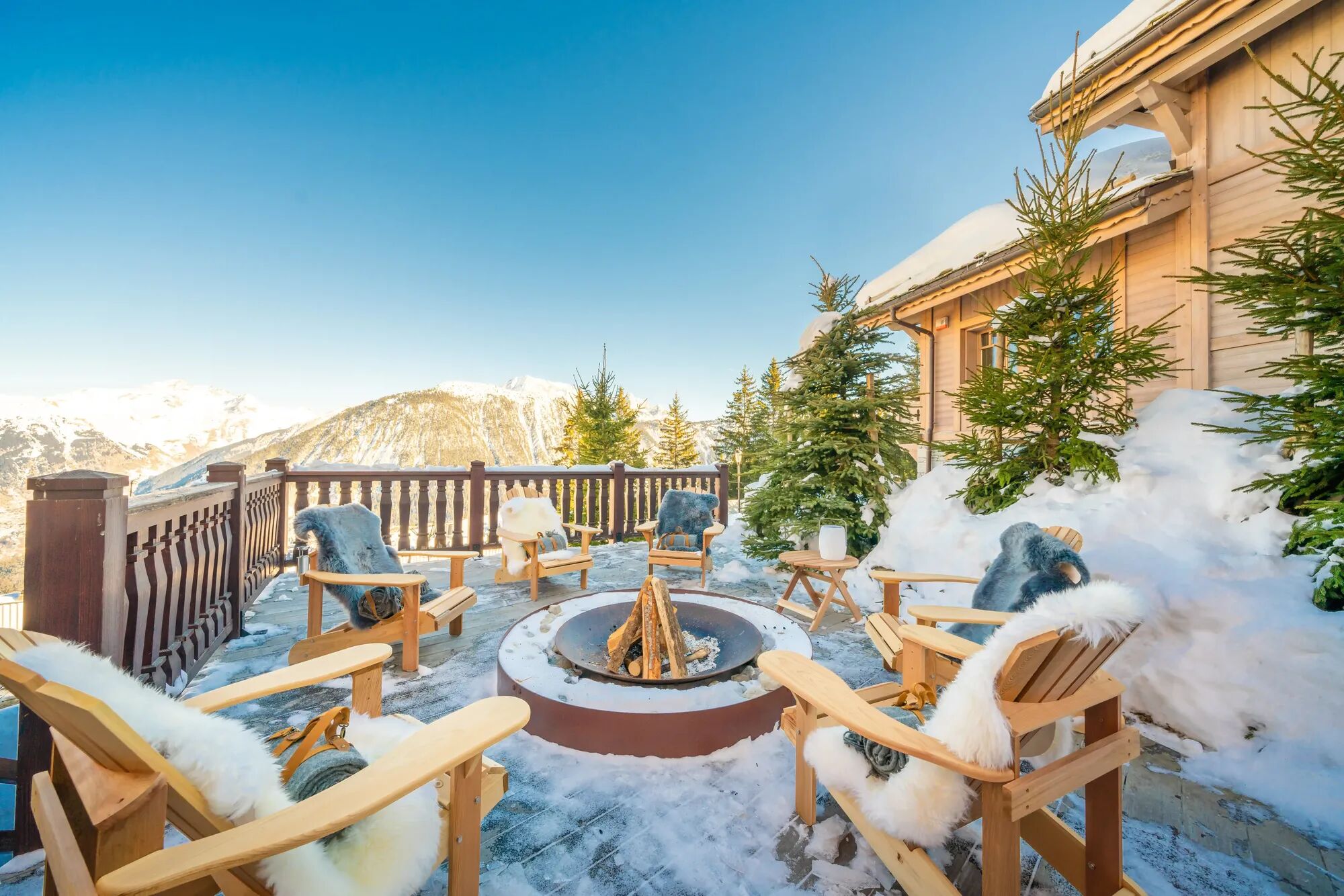 Exterior of luxury chalet rental with a beautiful firepit and chairs surrounding the snowy landscape.