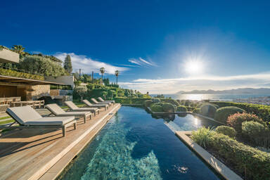 Sunlit pool deck at Villa Emerald with multiple loungers, stylish stone architecture, and breathtaking views across the French Riviera coastline