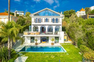 Symmetrical façade of Villa Nirvana with arched windows, lush garden, and central pool offering a peaceful escape in the heart of the French Riviera