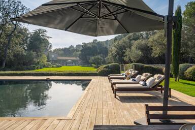 Wooden poolside terrace at Villa Paradis featuring sun loungers, parasols, and tranquil views across landscaped gardens and cypress trees