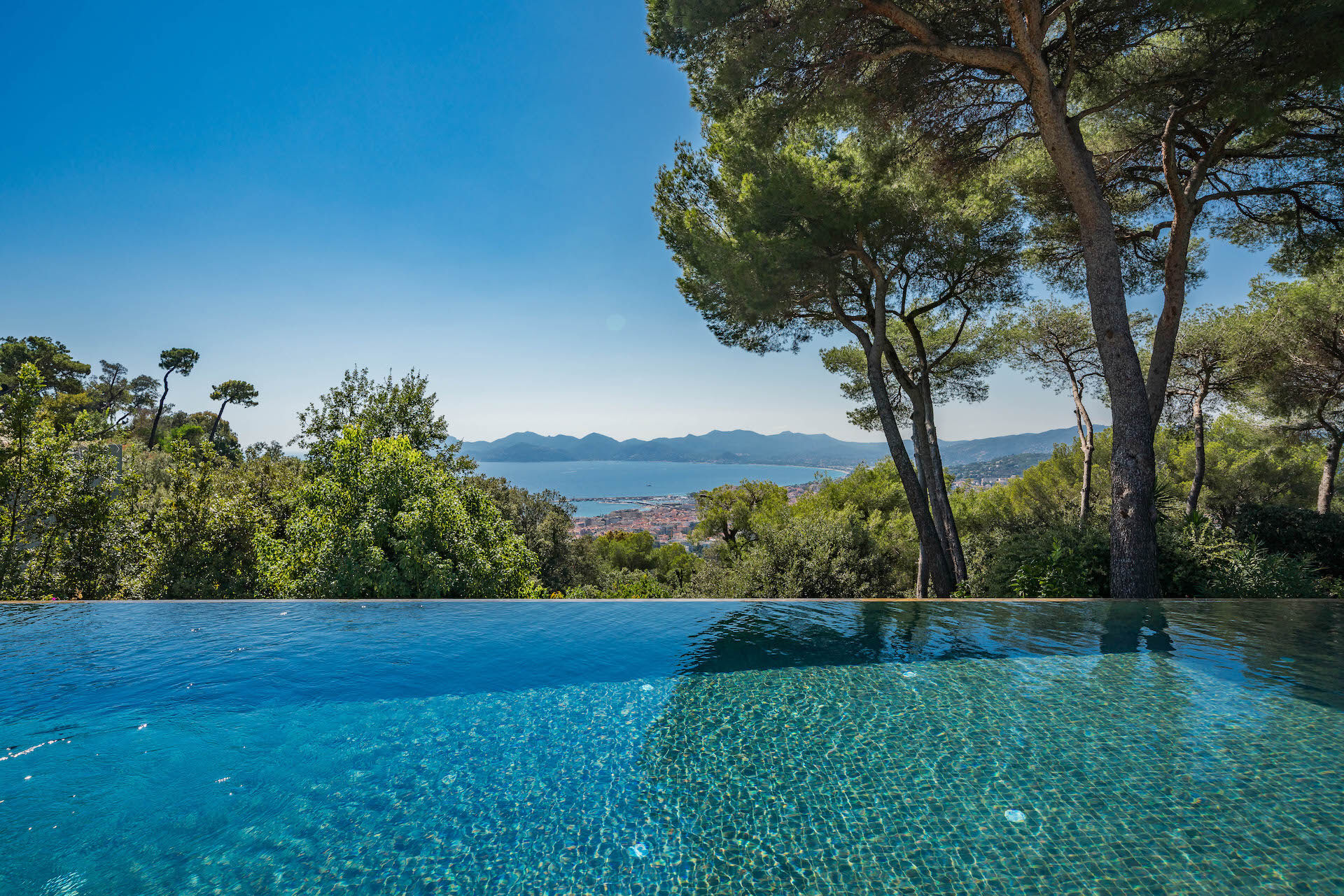 Infinity pool at Villa Phoenix with uninterrupted views across the Mediterranean and Îles de Lérins, framed by pine trees and blue skies
