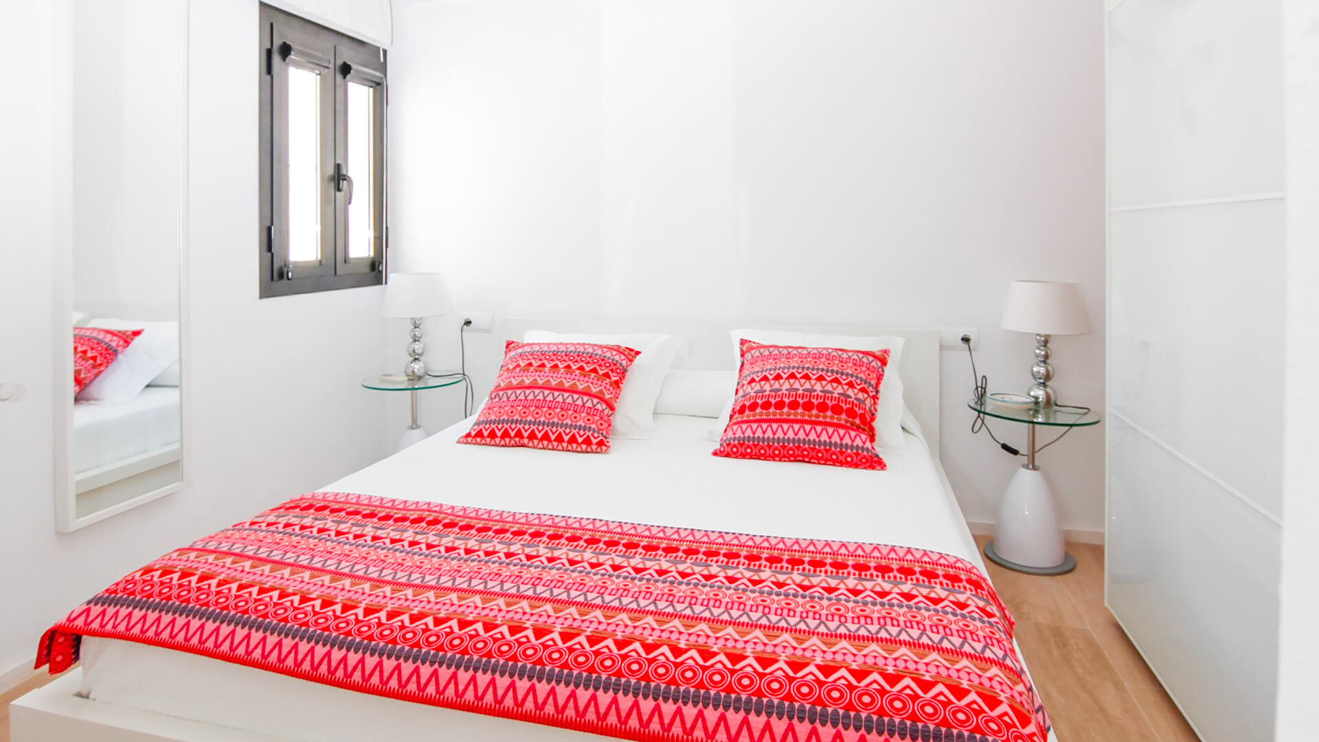 One of the large bedrooms in Can Bab in Ibiza, with white linens and a bold red throw.