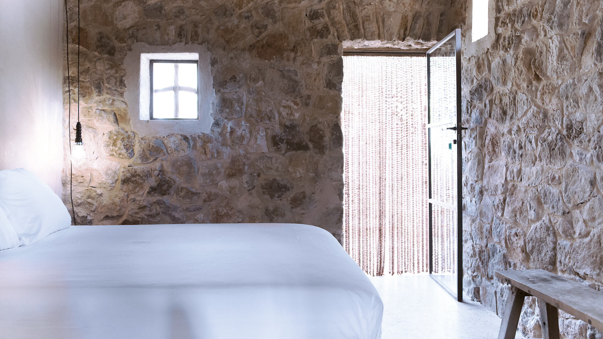 Close of the crips white bed linen and the opened door at Villa Can Basso in Ibiza