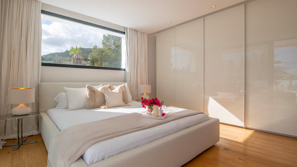 Bedroom with a giant window above the bed and built in wardrobes at Villa Casa Isa in Ibiza