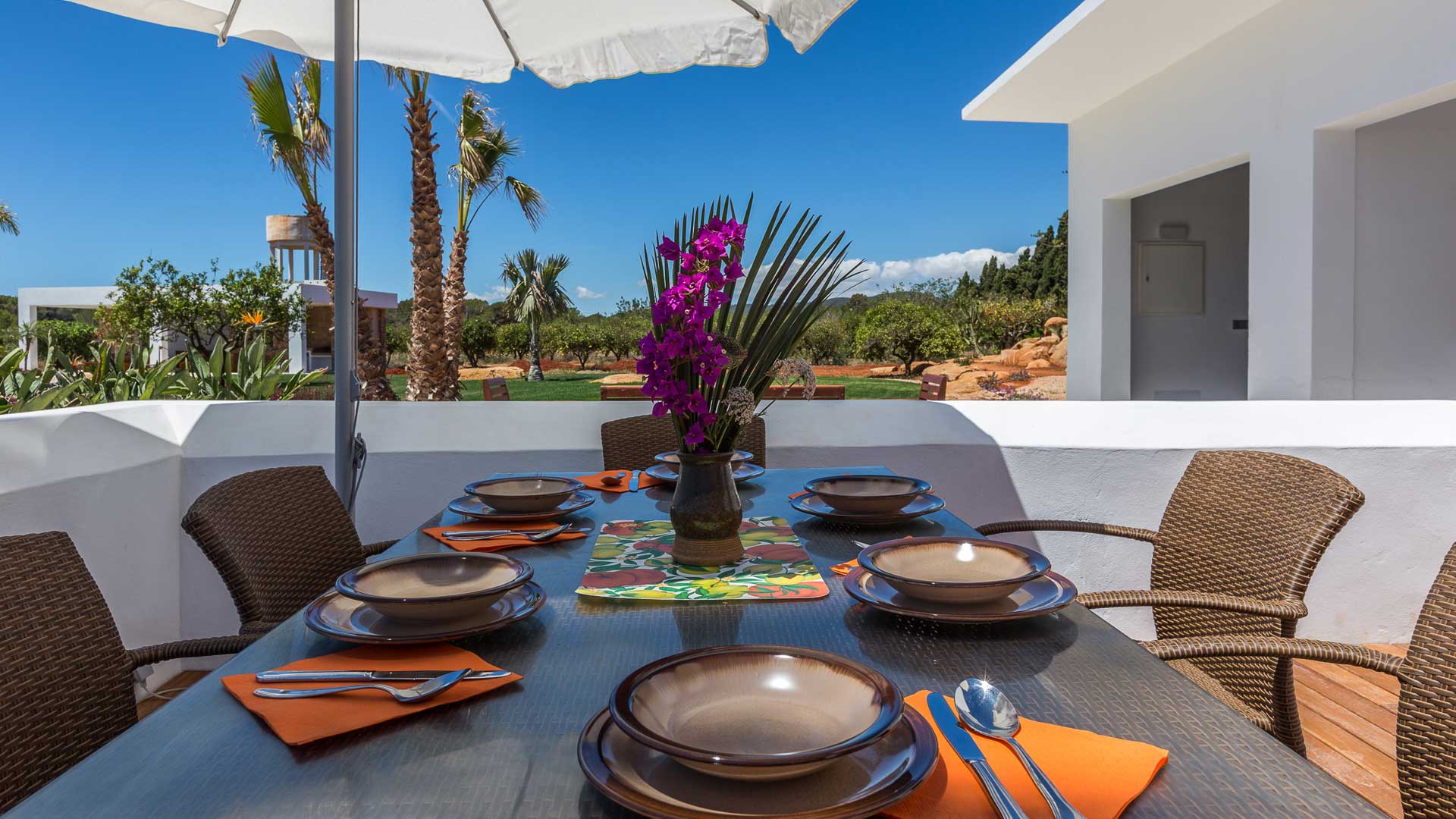 Shaded dining table at Villa Es Canar in Ibiza with pops of orange napkins