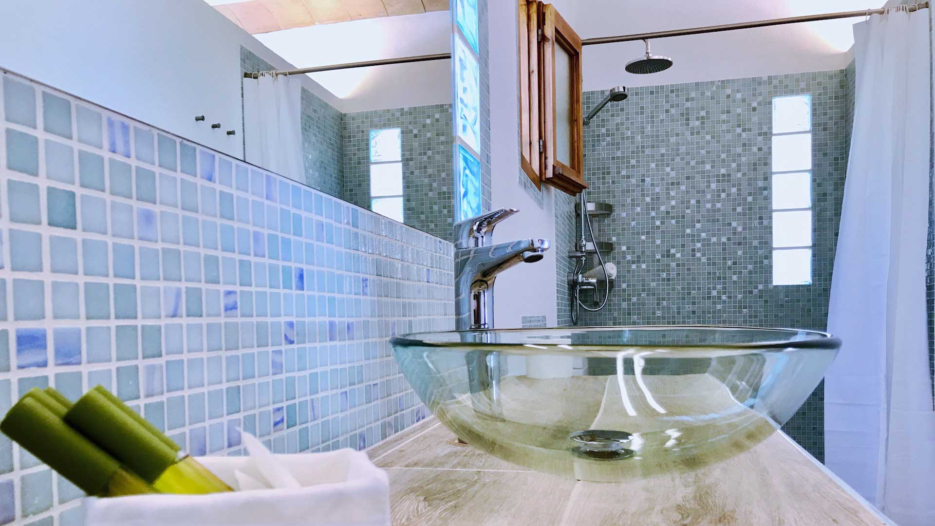 A tiled bathroom in Villa Payesa with transparent sink basins and skincare products