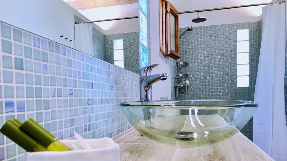 A tiled bathroom in Villa Payesa with transparent sink basins and skincare products