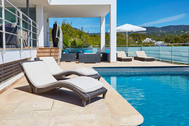 Sunloungers poolside at Villa White Beach in Ibiza with deep blue water
