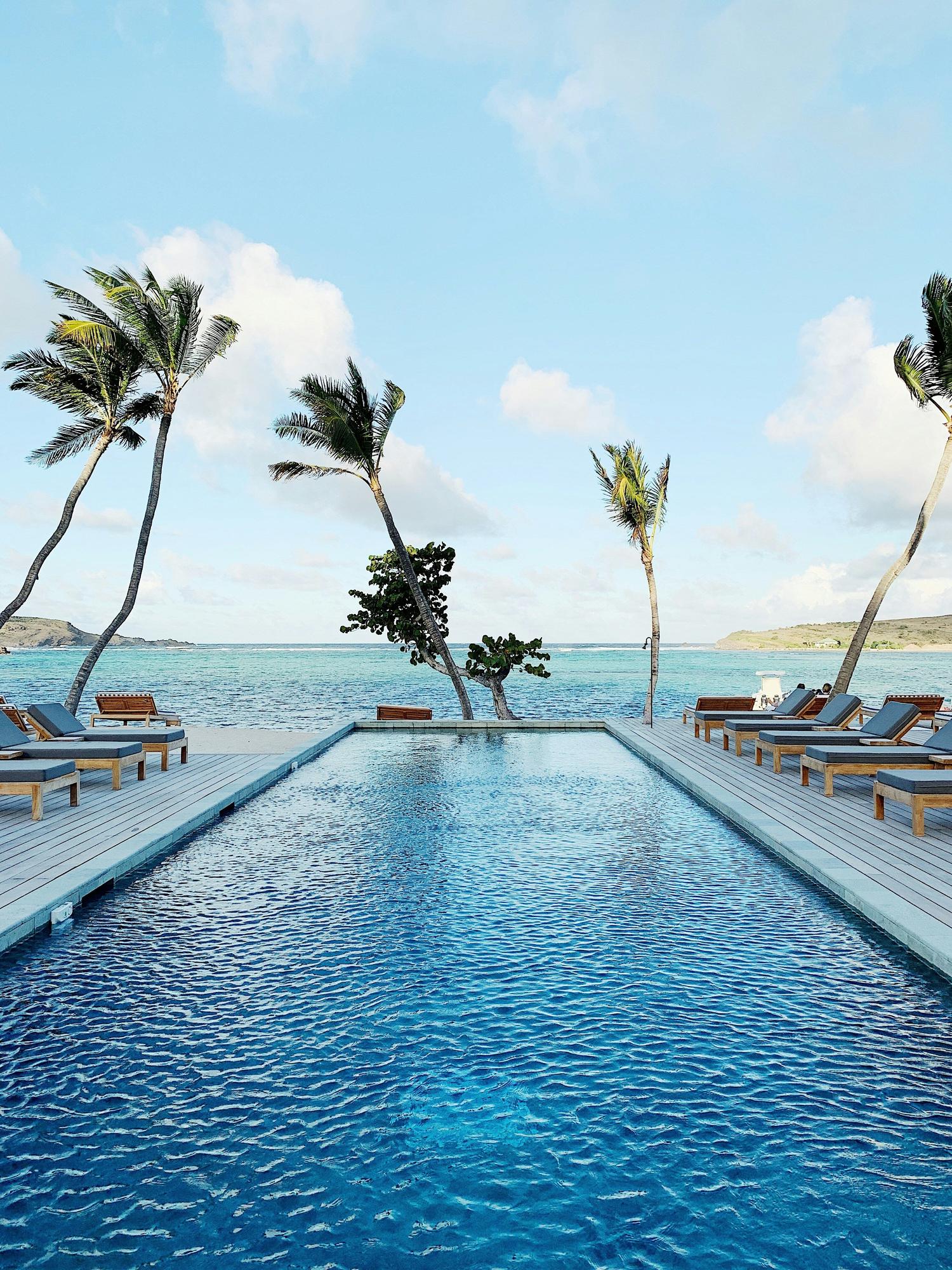 View of a pool that leads into the Caribbean Sea with palm trees swaying around