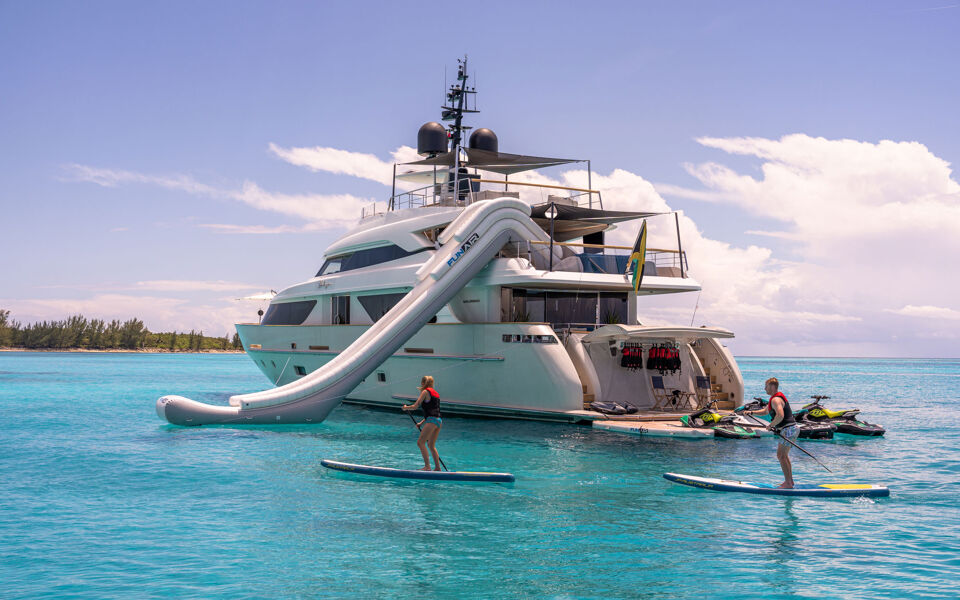 View of the aft of Halcyon at anchor with several charter guests paddleboarding around the motor yacht