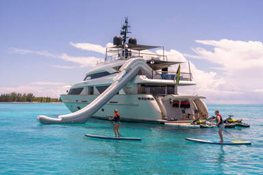 View of the aft of Halcyon at anchor with several charter guests paddleboarding around the motor yacht
